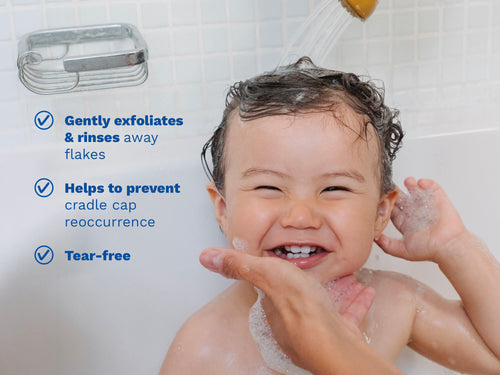 Smiling child in the bath with water running over their hair, while an adult gently supports their chin; blue text appears on the left side. - Mustela USA - 4