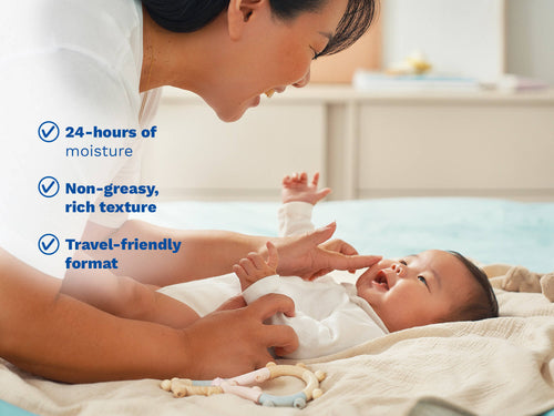 Parent leaning over and caring for a baby lying on a blanket, with blue text on the left side. - Mustela USA - 4