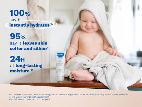 Baby sitting on a wooden surface wrapped in a towel, with a tube of Mustela cream in front and blue text on the left side. - Mustela USA - 2