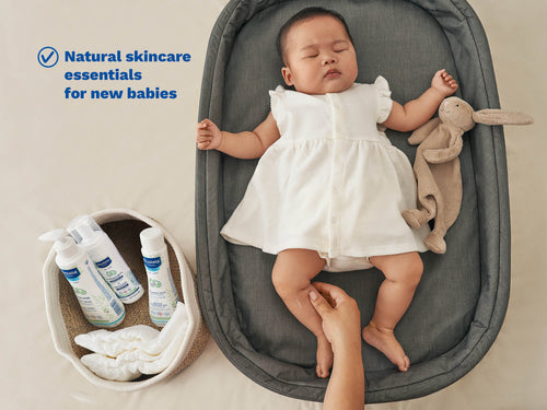 Mustela USA | Baby in a white dress lying on a gray mat with natural skincare products nearby. - Mustela USA - 2