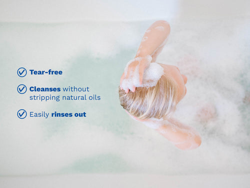 Child in a bubble bath washing their hair with foamy shampoo, with blue text on the left side. - Mustela USA - 4