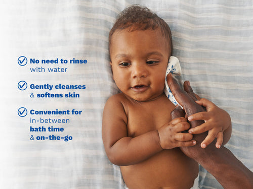 Mustela USA | Baby lying on a striped blanket while a parent wipes their cheek. - Mustela USA - 4