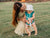 mom sitting in grass holding child and bottle of arnica gel