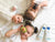 Image of 3 children laying down. Two of the children are holding avocados. 2 Bottles of Hydra Bebe Body Lotion next to them